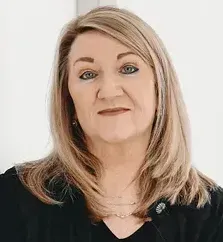 A woman with long red hair is smiling in front of a beach background