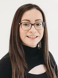 A man in a blue shirt and jeans is standing with his hands in his pockets.
