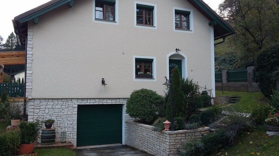 Ein Haus mit einem grünen Garagentor und einer Steinmauer