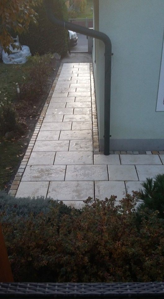 Ein Gehweg, der zu einem Haus führt, an dessen Seite sich ein Abflussrohr befindet.