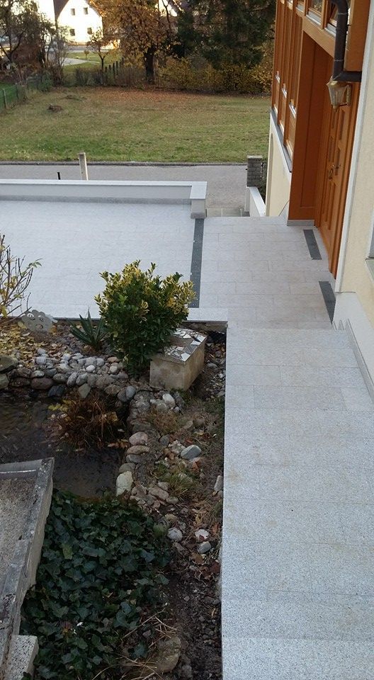Ein Betonweg führt zu einem Haus mit einem Garten davor.
