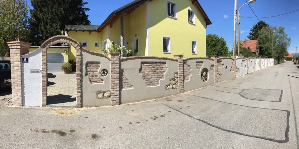 Ein gelbes Haus mit einem Backsteinzaun davor.