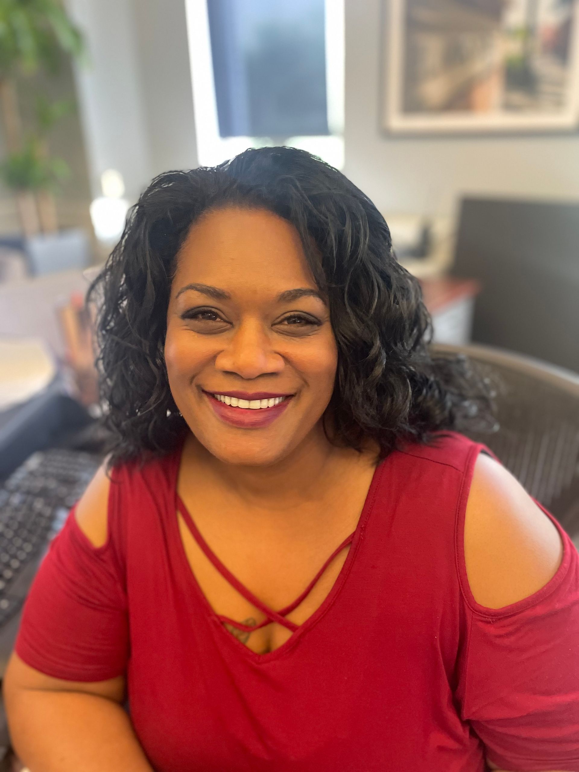a woman in a red shirt is smiling for the camera while sitting in a chair .