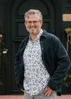 Arek Reeder, A man with a beard and glasses is standing in front of a black door.