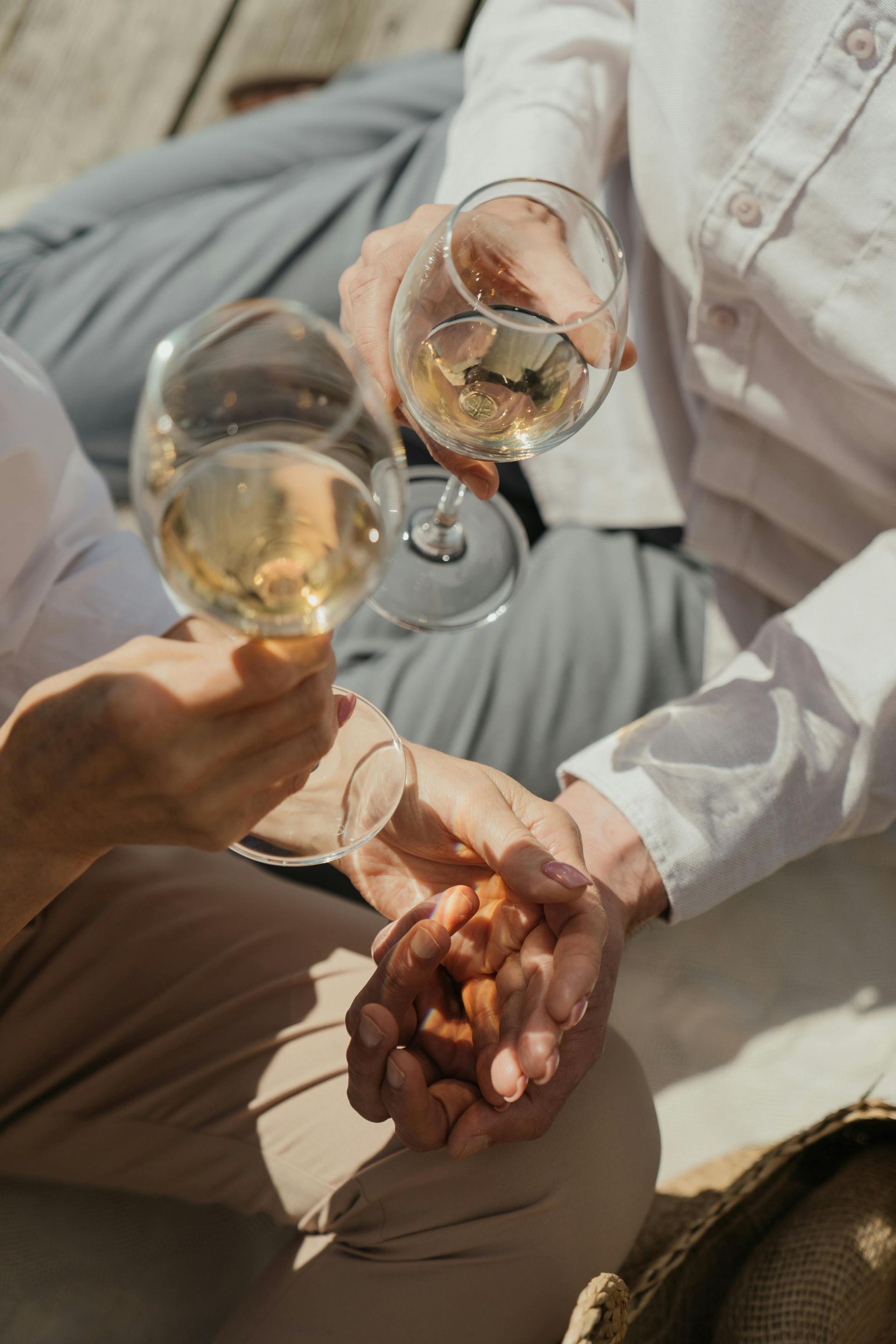 Two people holding wine glasses, toasting outdoors, hands clasped.