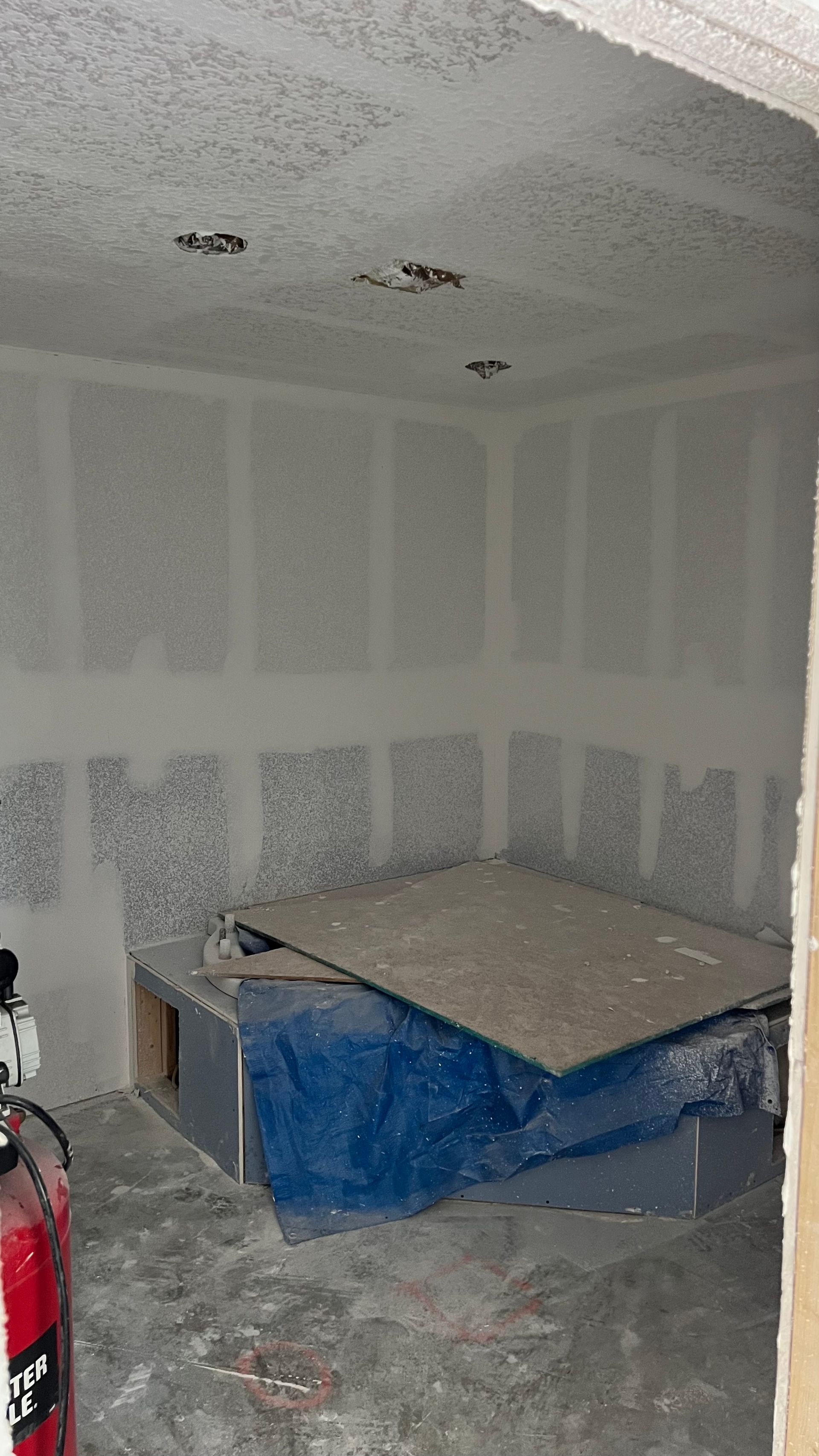 A room with a blue tarp on the floor and a fire extinguisher.