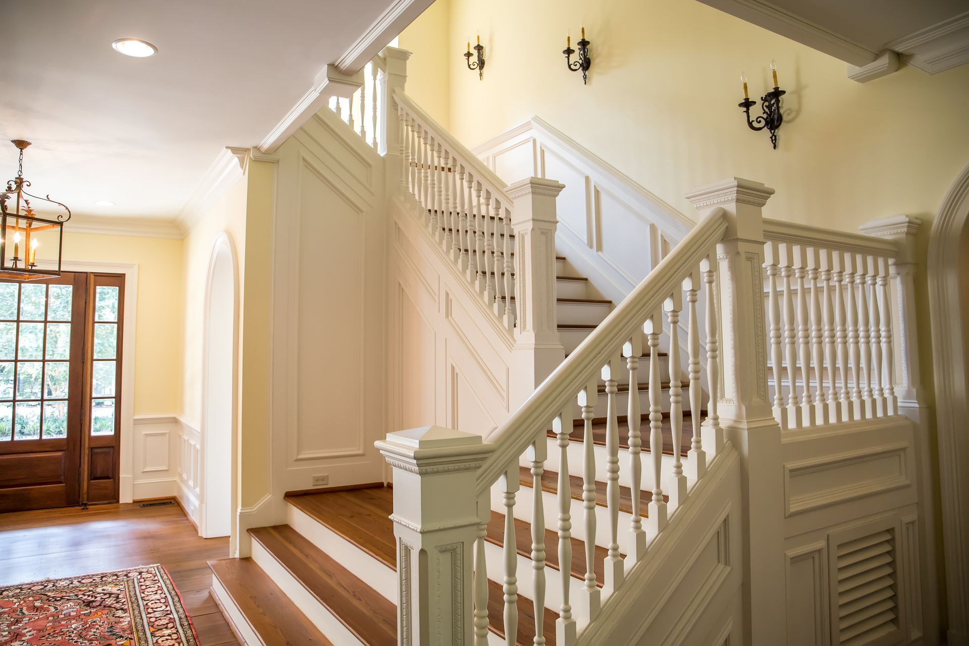 Bright foyer with a staircase, white railings, hardwood floors, and a front door with sidelights