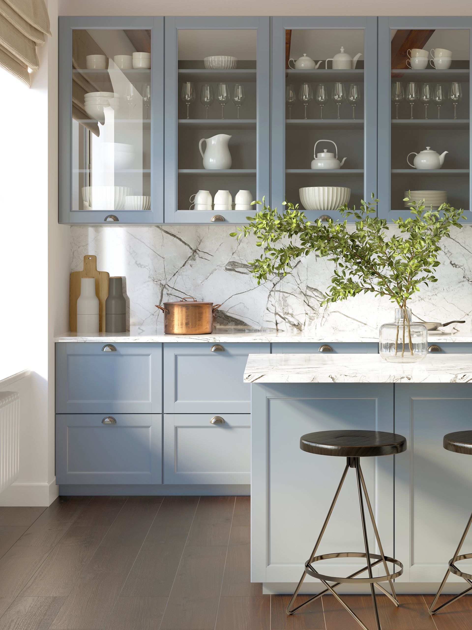 Light blue kitchen with glass cabinets, marble backsplash, and a small island with a stool and flowers.