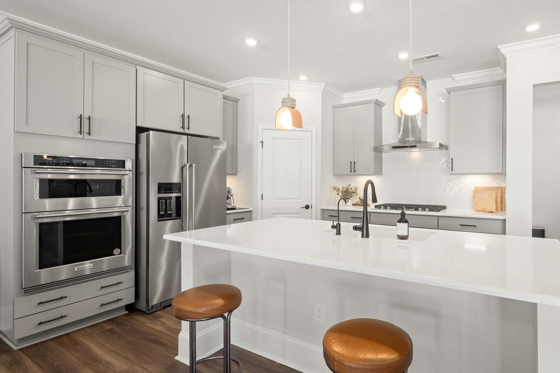 Modern white kitchen with island, stainless steel appliances, pendant lights, and two stools