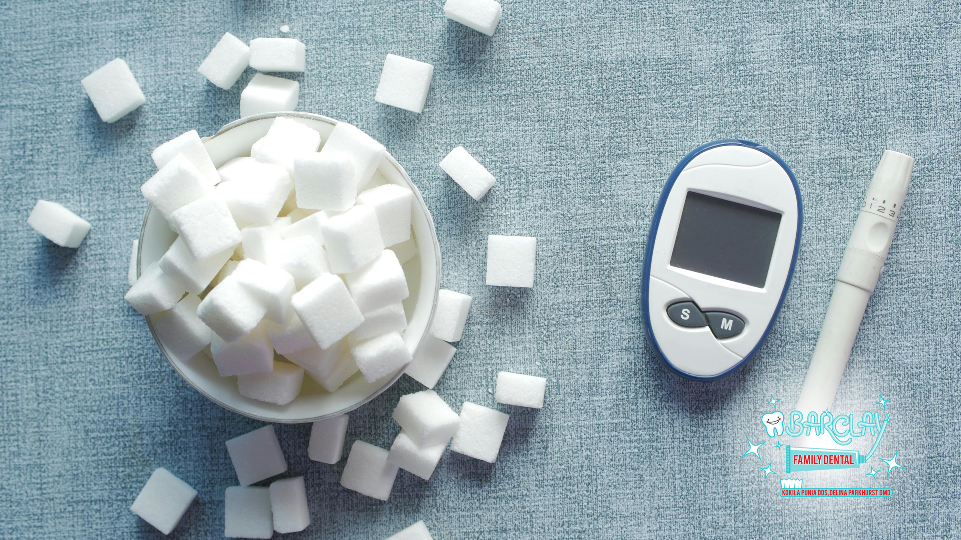 Bowl of sugar cubes with a blood glucose monitor and a lancet on a blue surface.