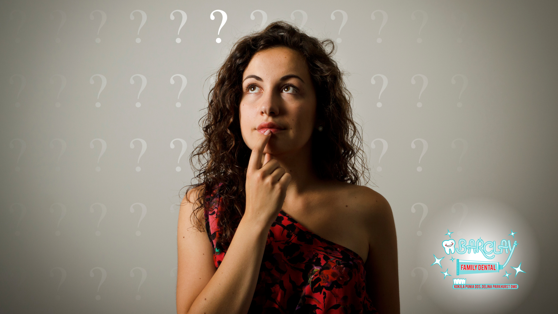 A woman in a red dress is thinking in front of a wall with question marks.
