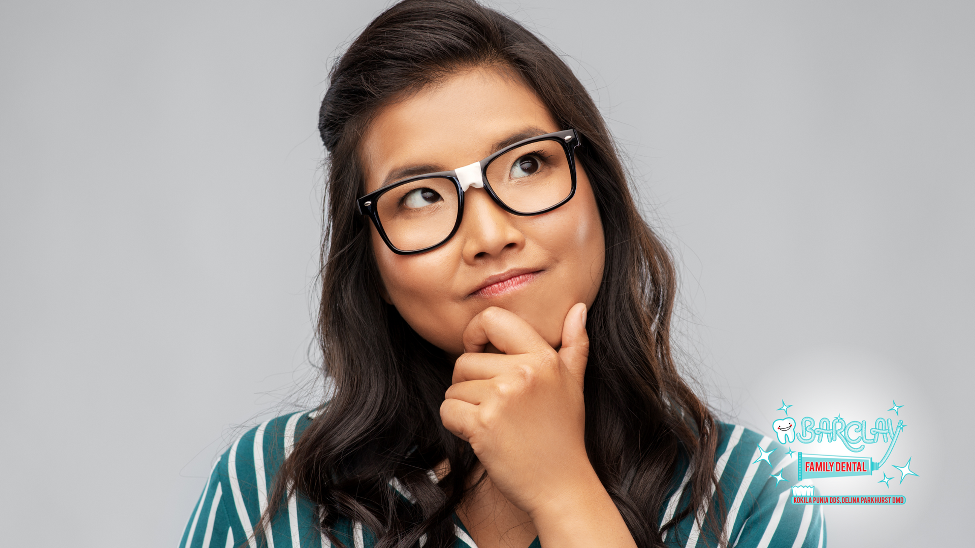 A woman wearing glasses is thinking with her hand on her chin.