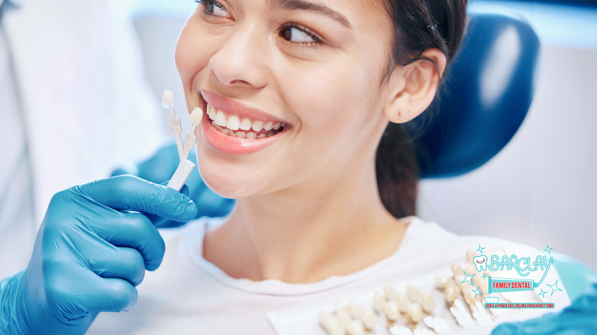 Woman smiling as dentist compares tooth shade with samples in dental office.