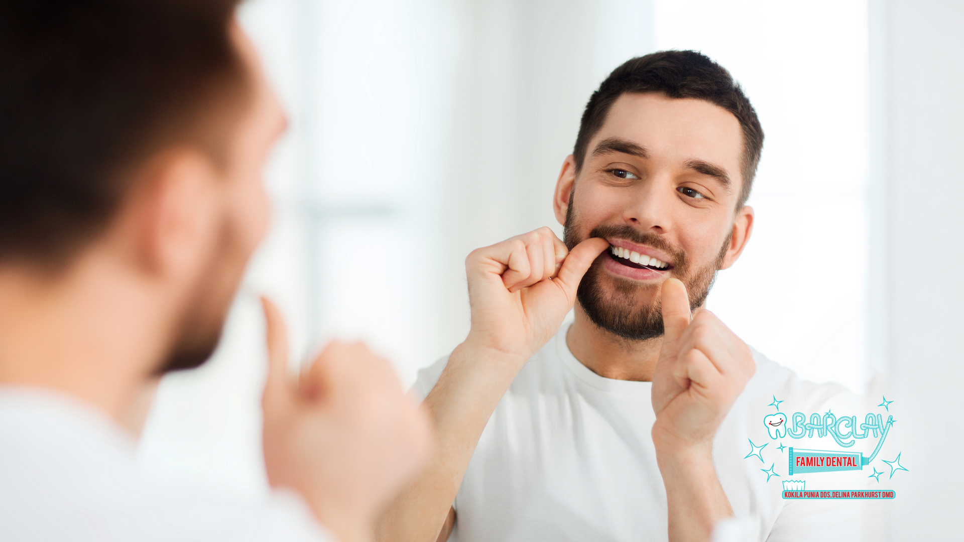 A man is flossing his teeth in front of a mirror.