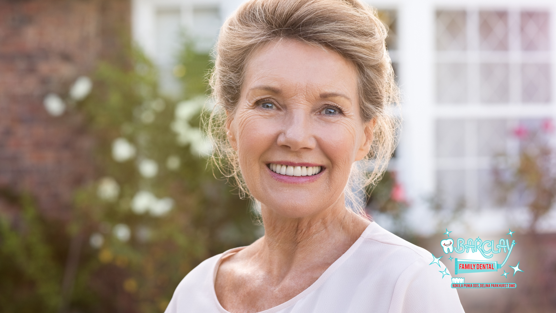 Woman with fair skin smiles outdoors in front of a house.
