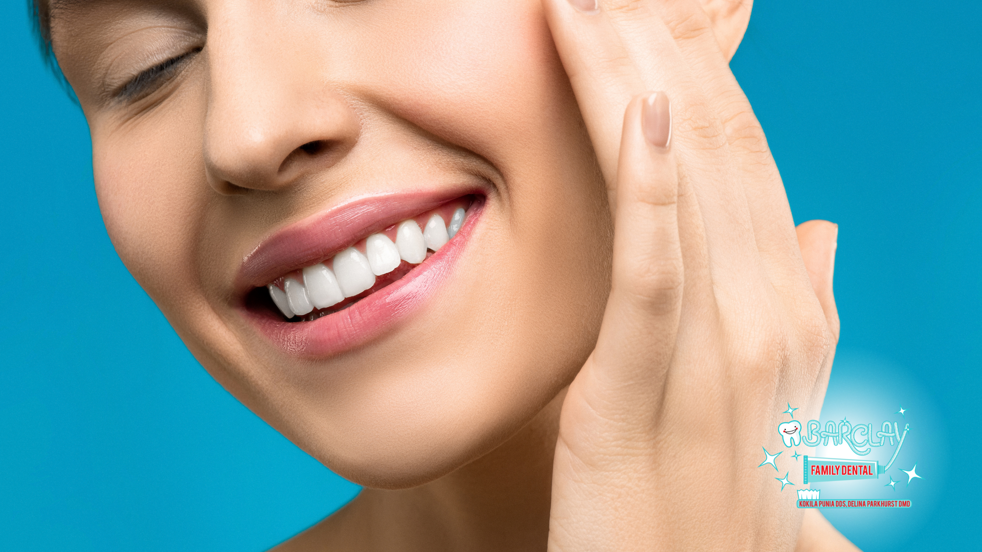 A woman is smiling and touching her face with her hand.