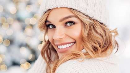 a woman wearing a hat and sweater is smiling in front of a christmas tre | Barclay Family Dental | Best Dentist For Family Dentistry, Dental Implants, and Cosmetic Dentistry in Cherry Hill, NJ