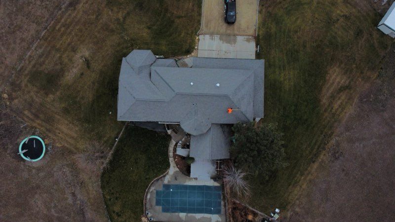 Snow-covered single-story house with stone facade, dark roof, and surrounding trees.