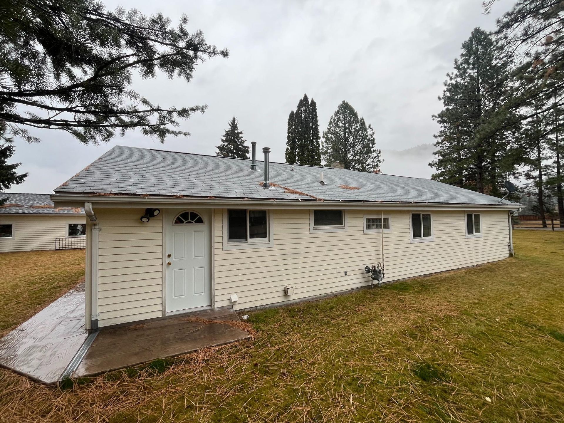 Tan building with gray roof, door, windows, and surrounding trees under overcast sky.