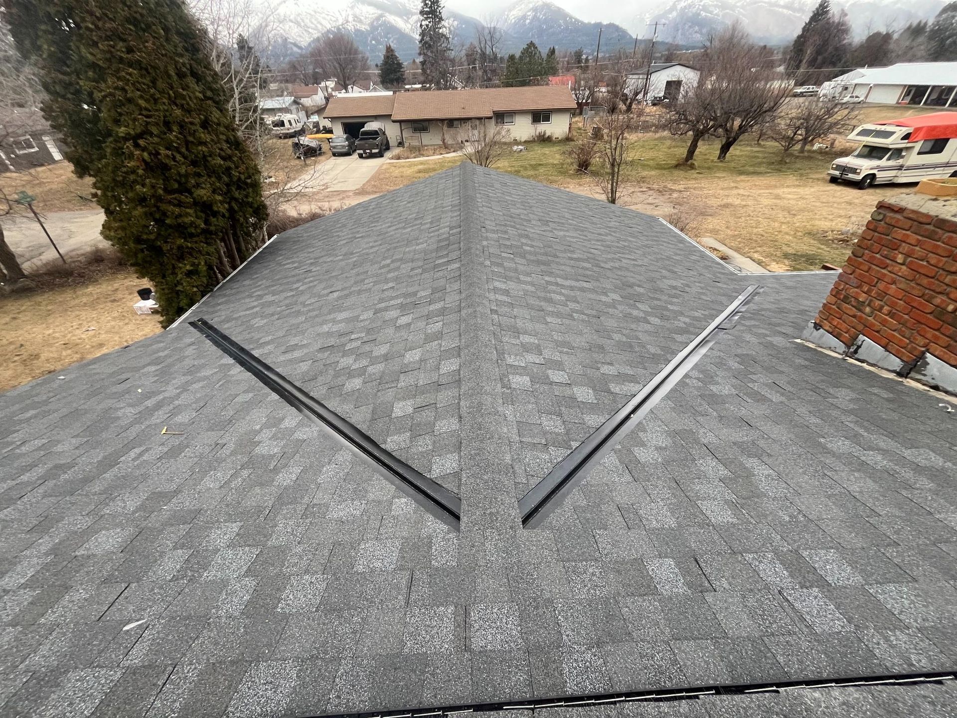 Gray shingle roof with black flashing, mountain backdrop, overcast day.