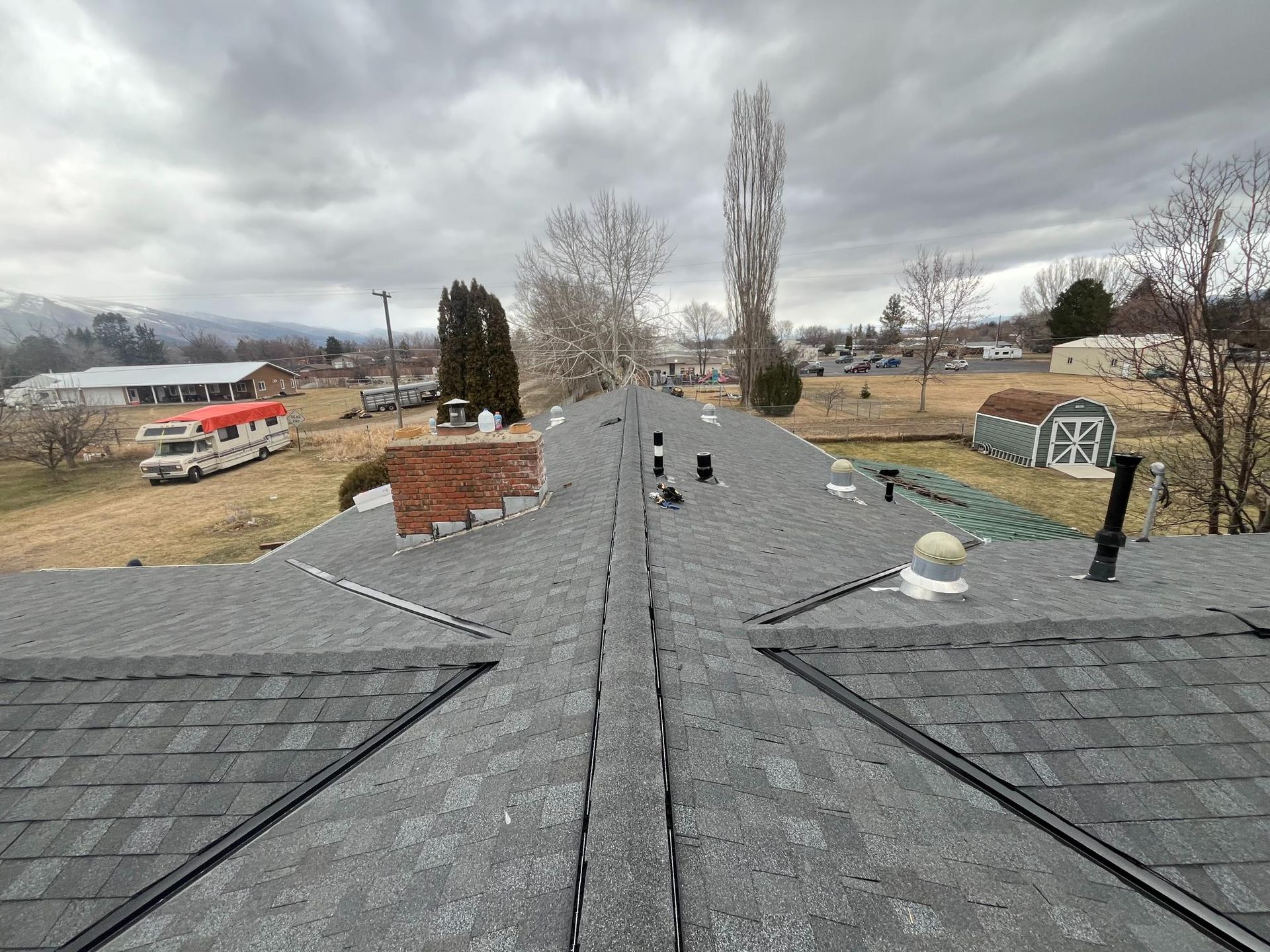 View of a newly shingled roof with various vents, chimneys, and an overcast sky.