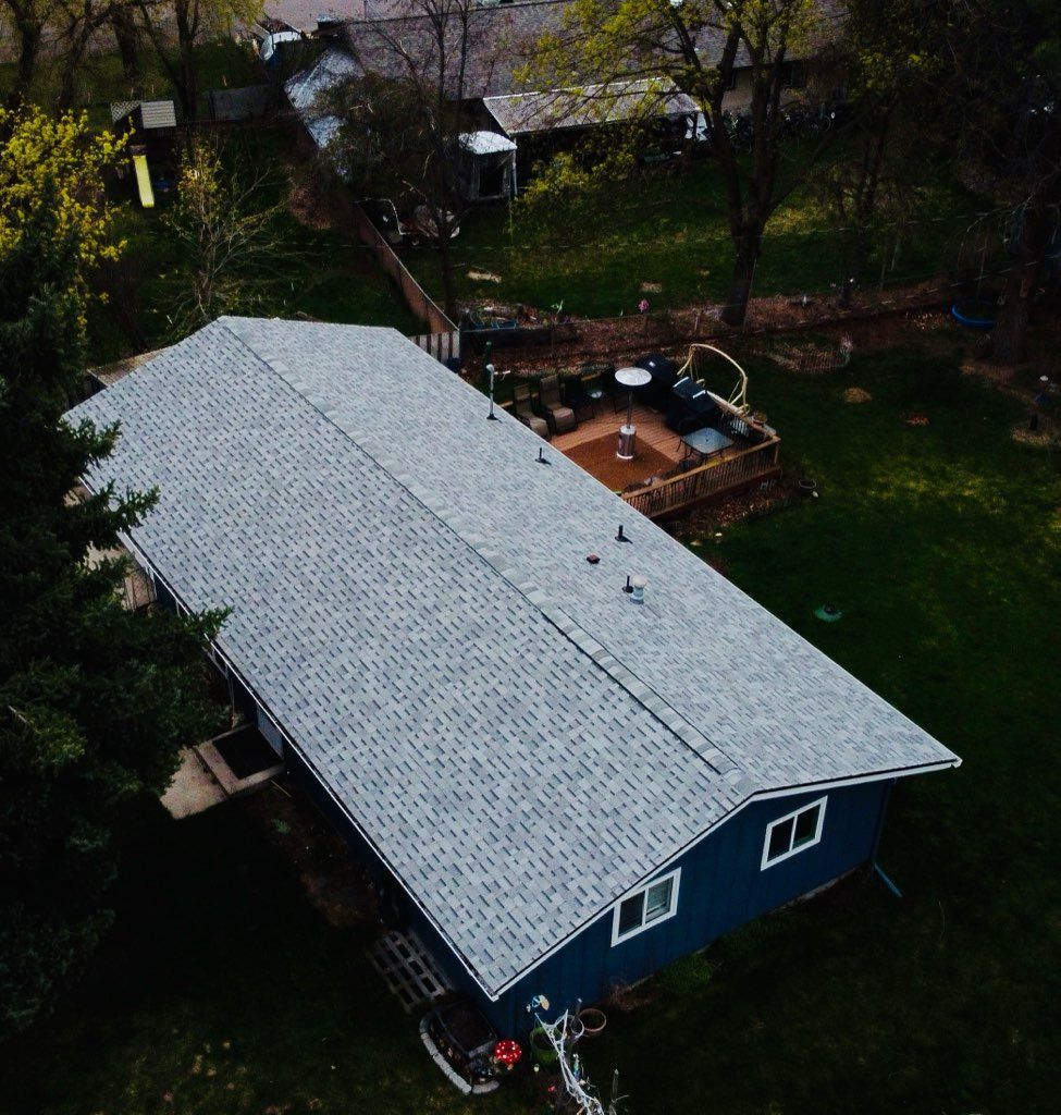 Aerial view of a blue house with a gray roof, surrounded by trees and a backyard patio.