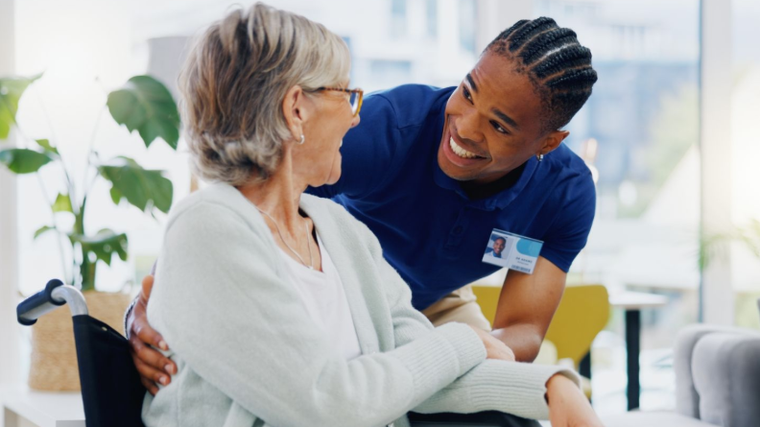 Nurse in blue uniform warmly talks with a seated patient in a bright clinic.