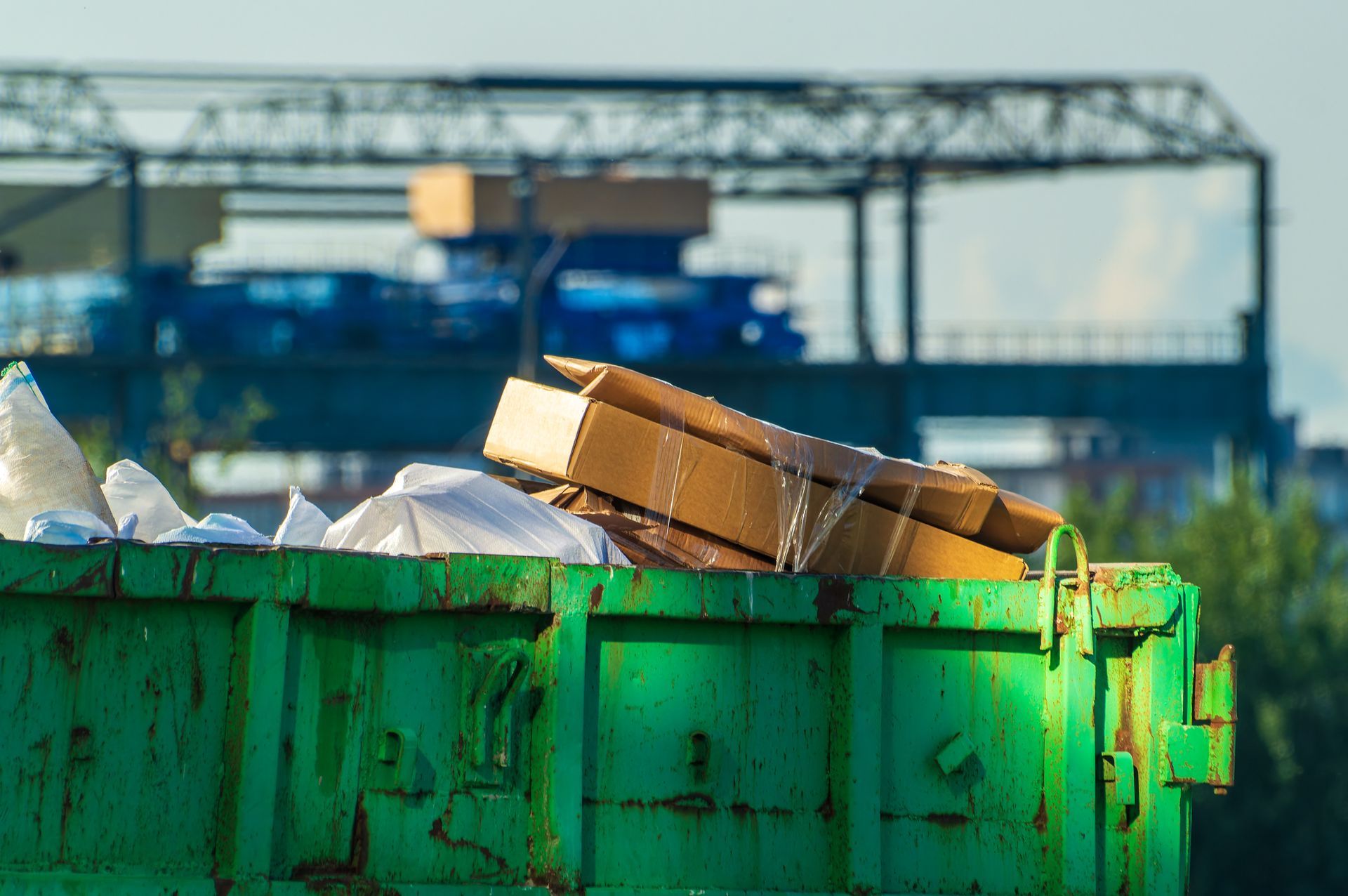 A green dumpster filled with cardboard boxes and plastic bags.