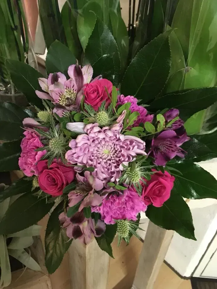 Buket af lyserøde og lilla blomster med grønt løv på en træoverflade.