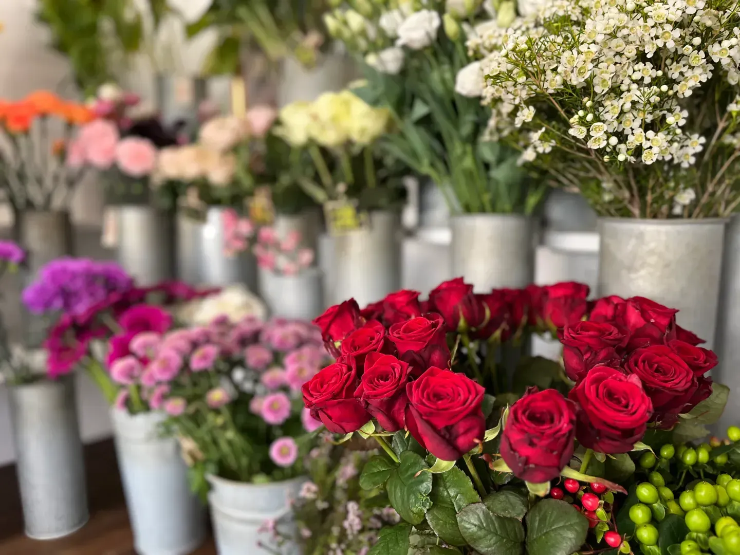 To buketter af hvide og lyseblå blomster med grønne blade, bundet med blå bånd, på en træoverflade.