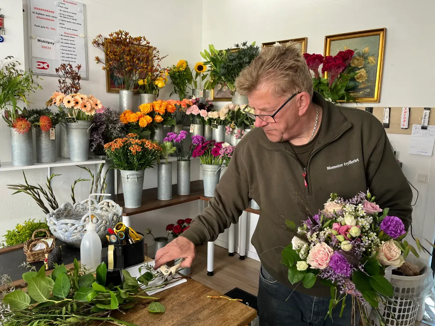 Blomsterhandler arrangerer en buket i en butik fyldt med farverige blomster.