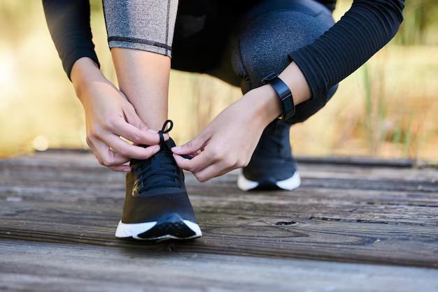 Persona atándose los cordones rosas de sus zapatos en un sendero de tierra, lista para correr.