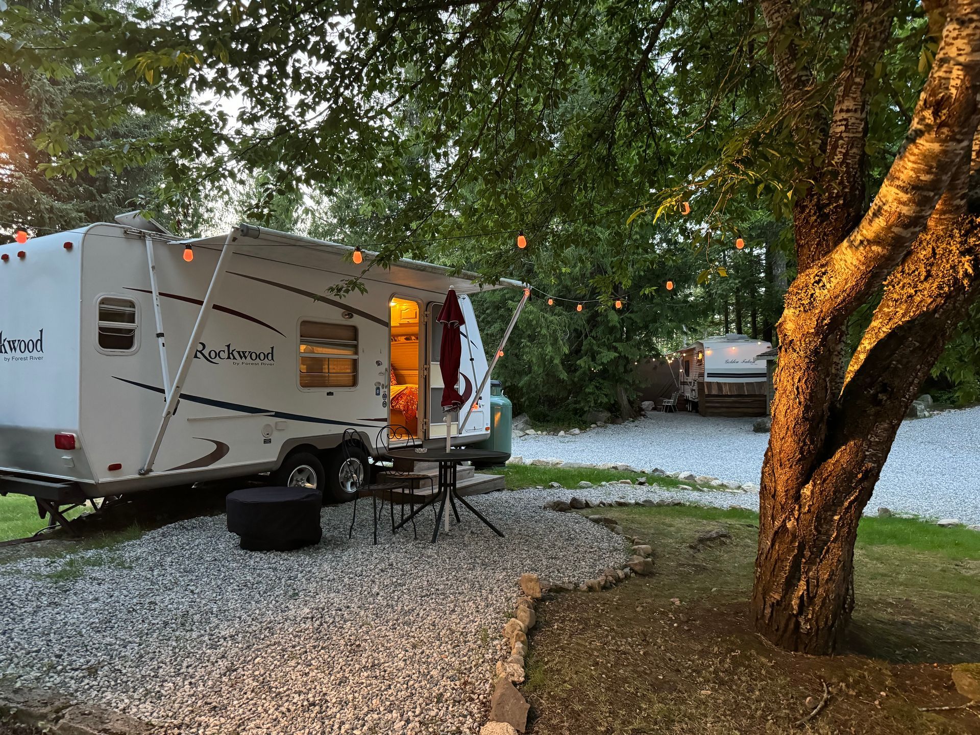 a group of people are sitting around a campfire in front of a trailer .