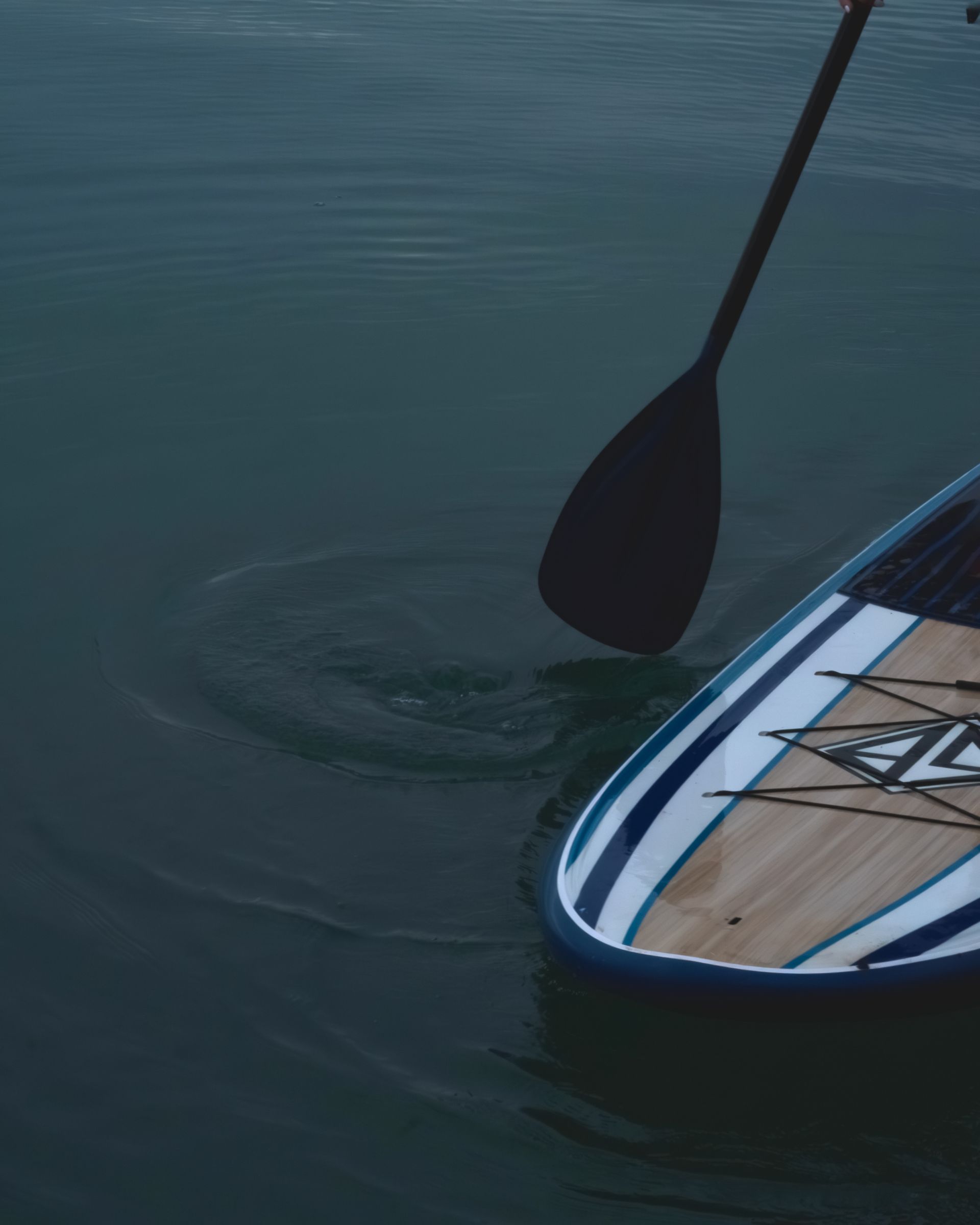 Paddleboard with blue and white stripes, paddle in water creating a swirl.