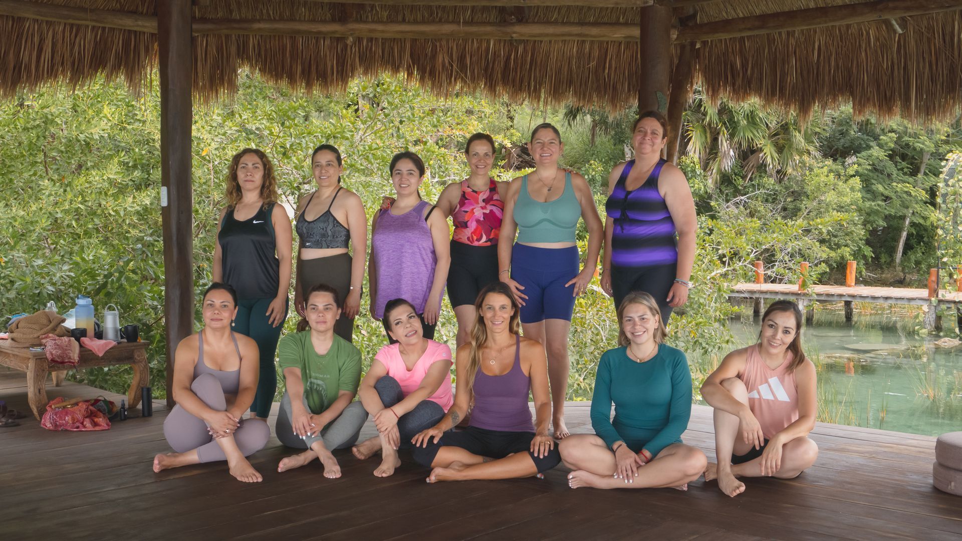 Group of women in workout clothes posing in a gazebo near water and trees.