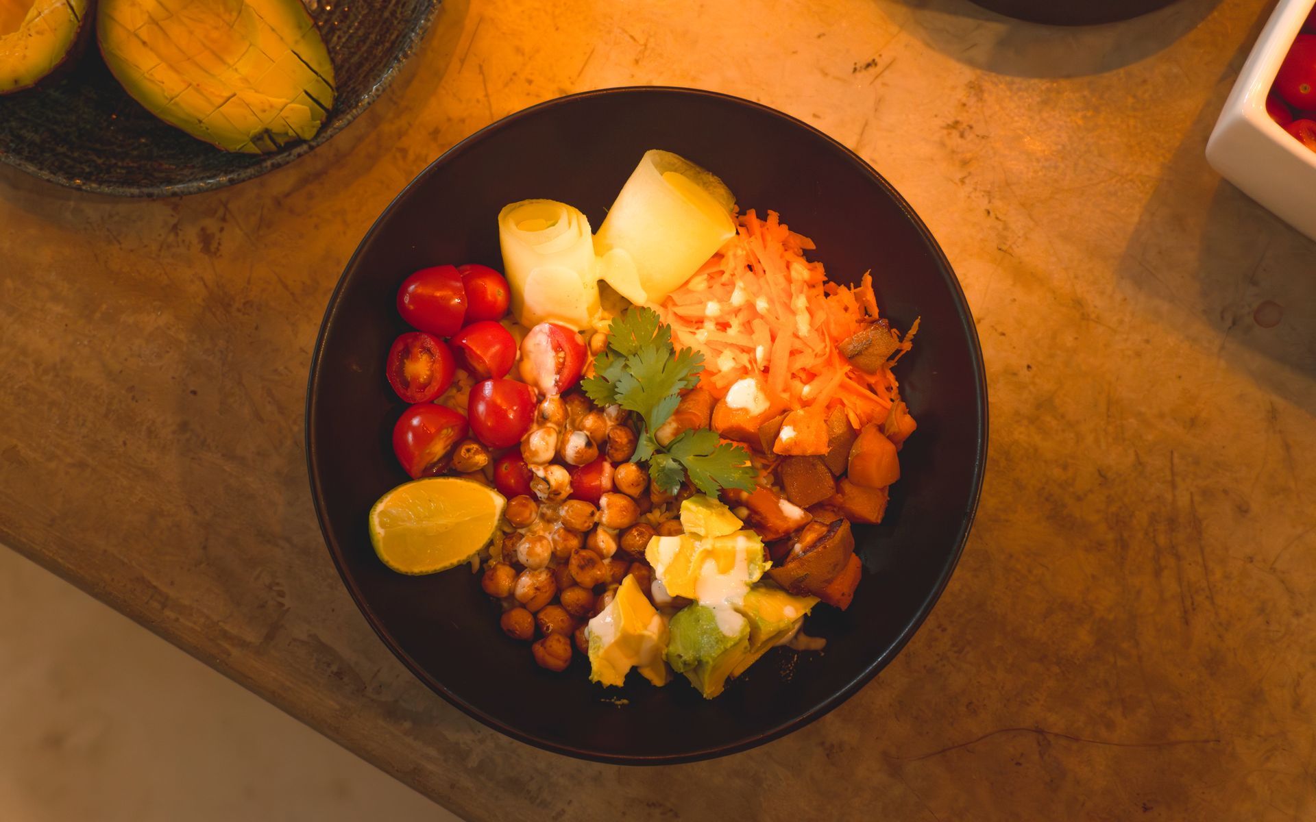 Black bowl filled with colorful vegetables, chickpeas, avocado, and lime on a wooden table.