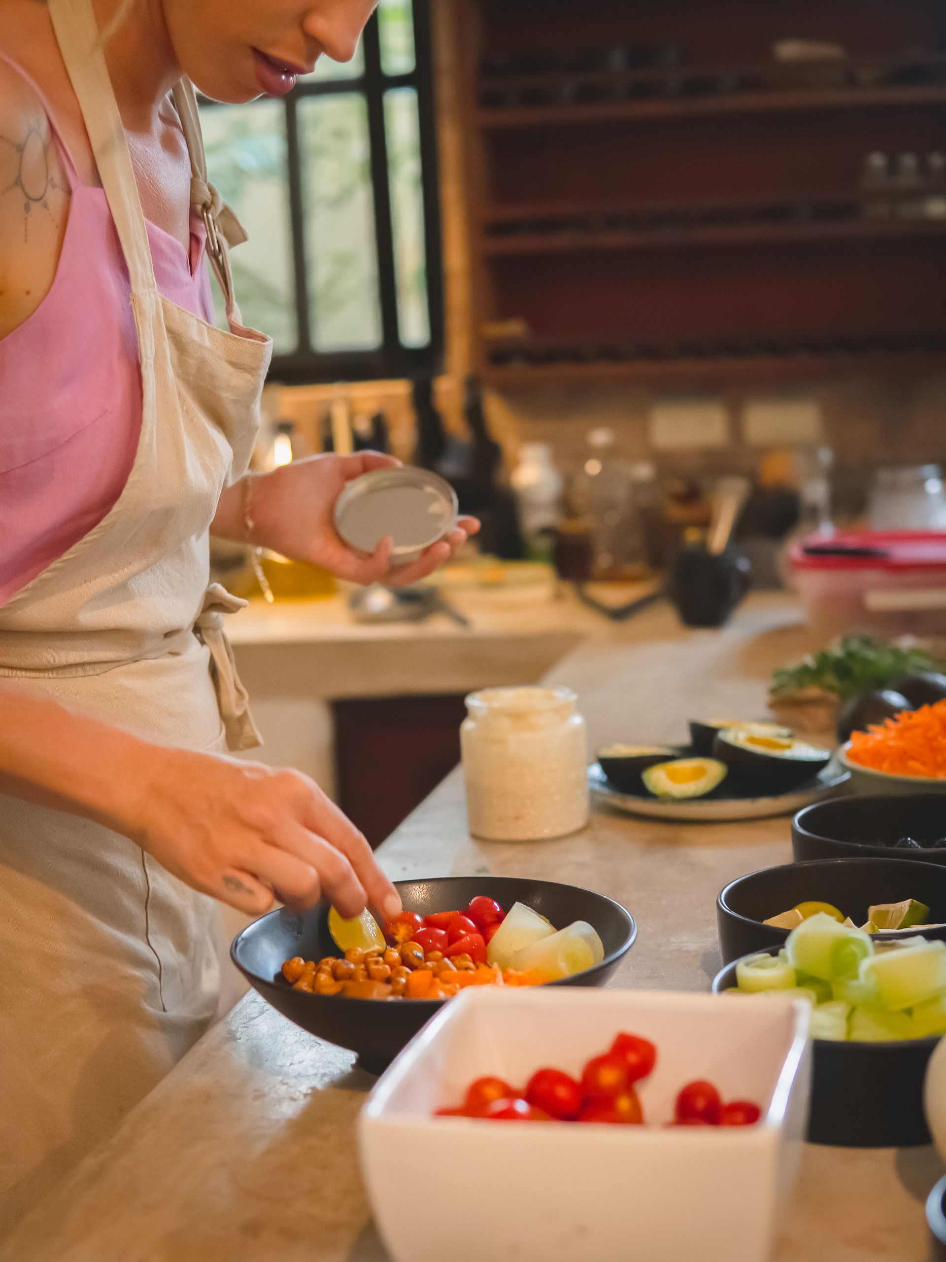Woman preparing a meal in kitchen. Adding ingredients to a bowl. Ingredients in various containers.
