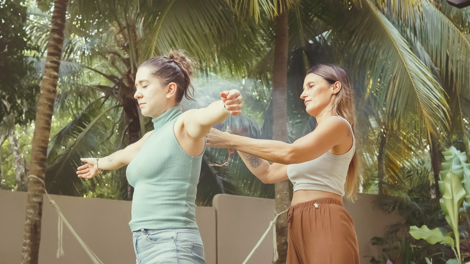 Silhouette of a person meditating with hands raised, sun shining above them; framed by trees.