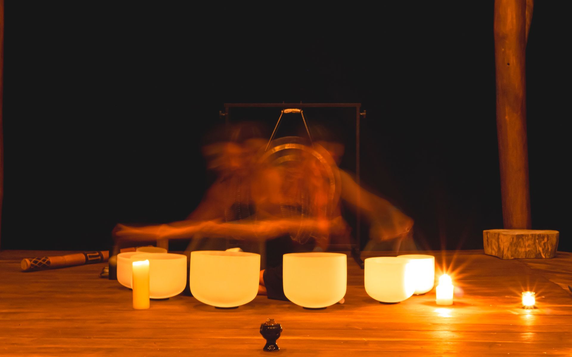 Person playing crystal singing bowls in a candlelit room. Blurred motion and warm tones.