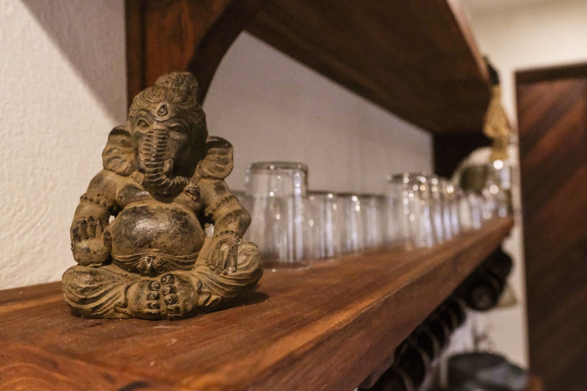 Statue of Ganesha on wooden shelf with glasses.