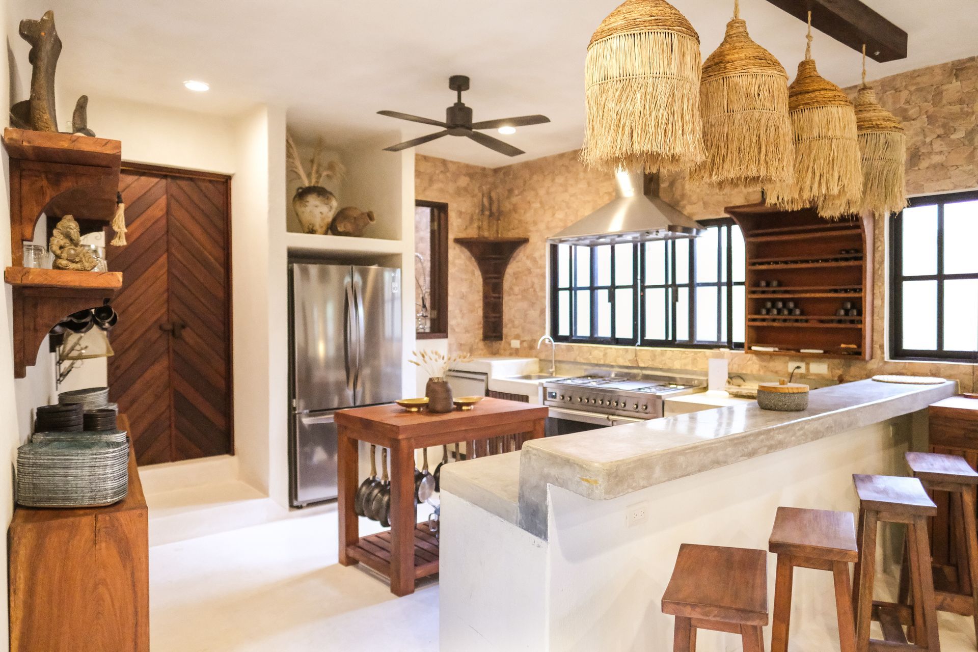 Rustic kitchen with stone wall, wooden cabinets, and woven pendant lights.