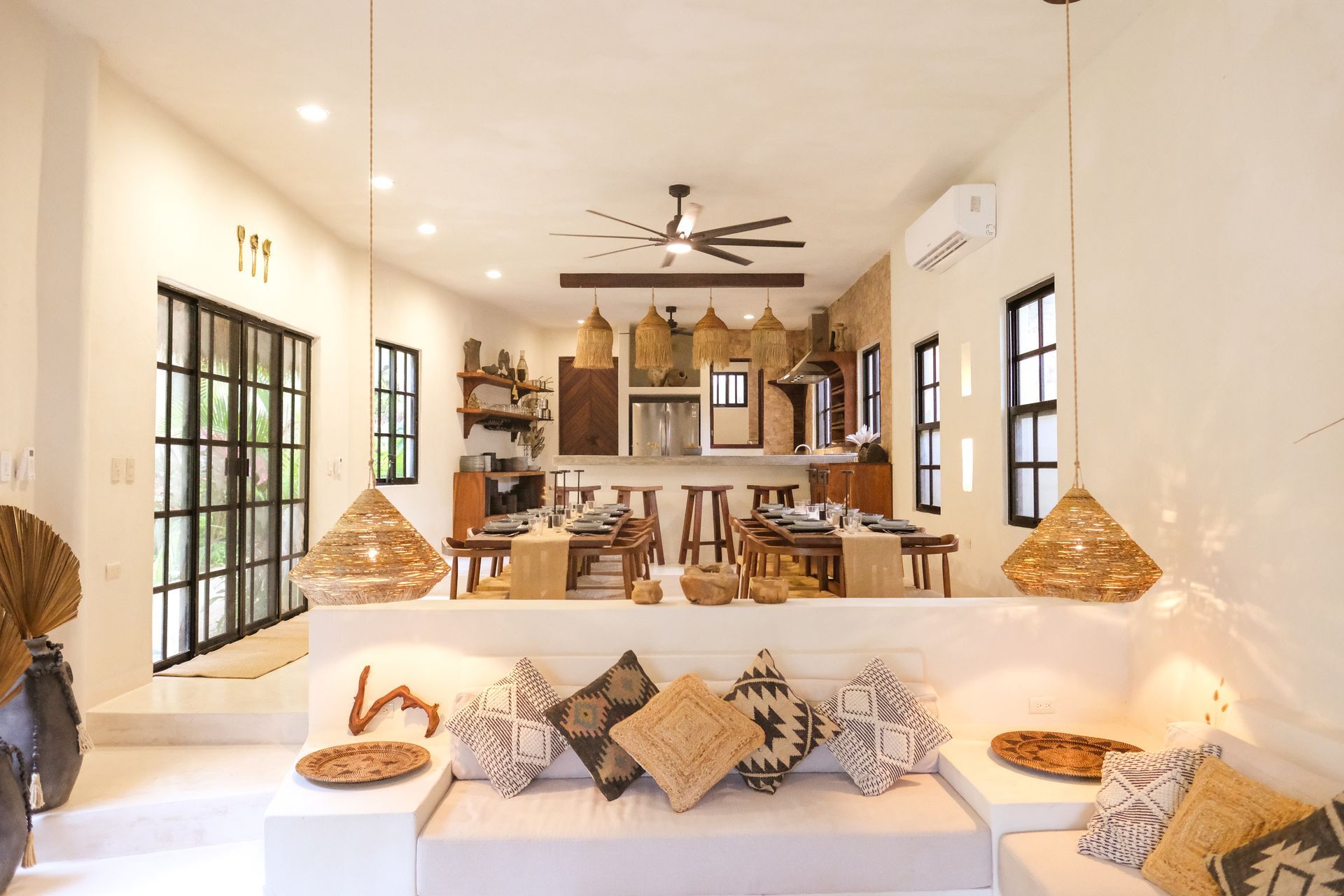 Bright, open-plan living space with raised seating area, dining table, and kitchen; neutral tones and decorative baskets.