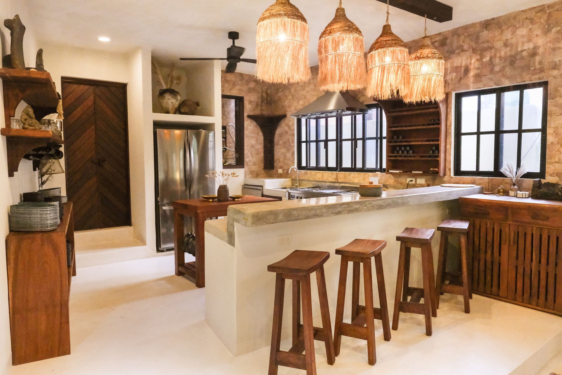 Kitchen with stone walls, island with stools, decorative lights, stainless steel appliances, and wooden accents.