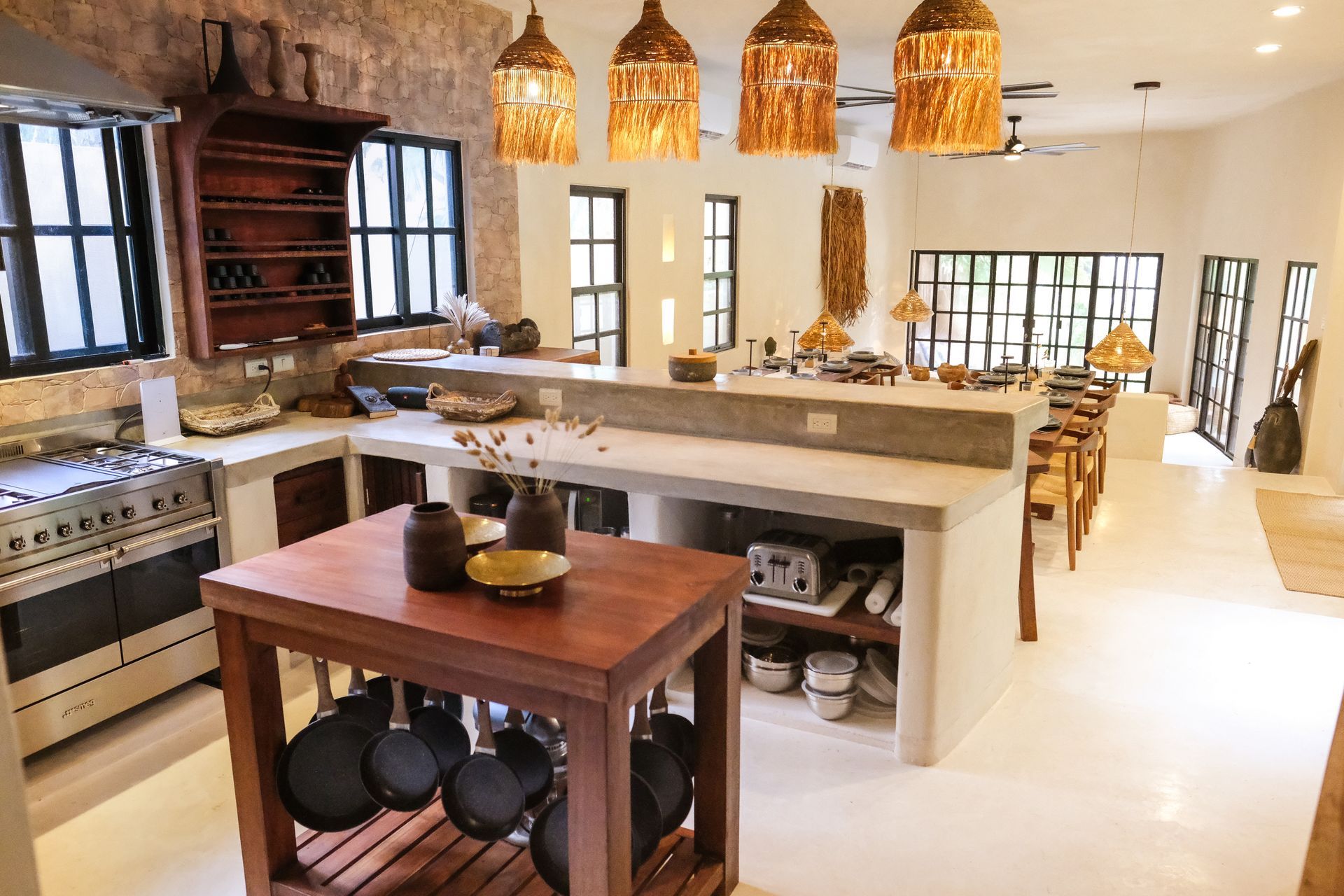 Bright kitchen with stone walls, large island, wooden cabinets, and hanging pots.