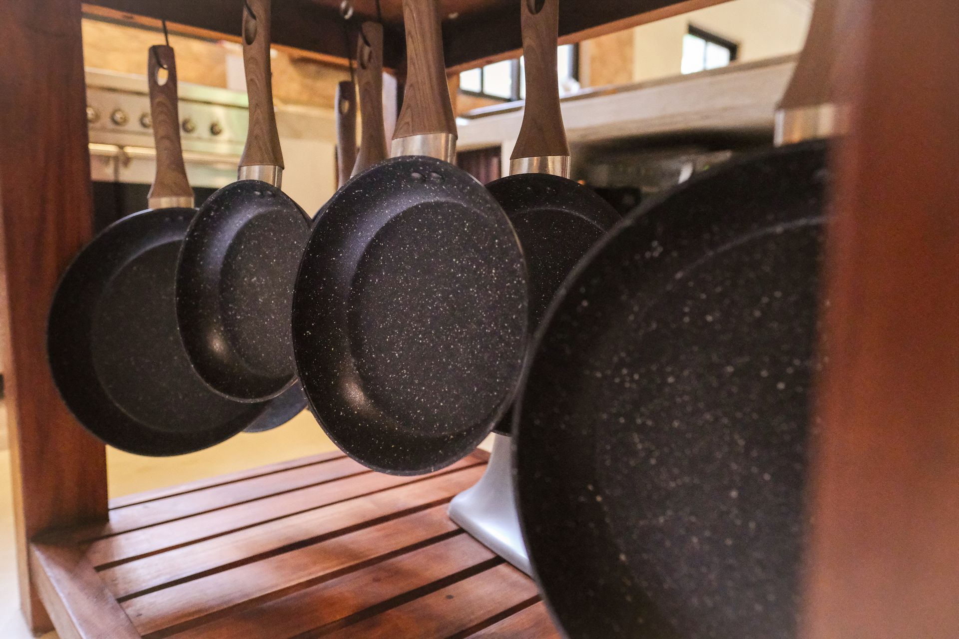Pans with speckled, dark-colored surfaces hanging on a wooden rack in a kitchen setting.