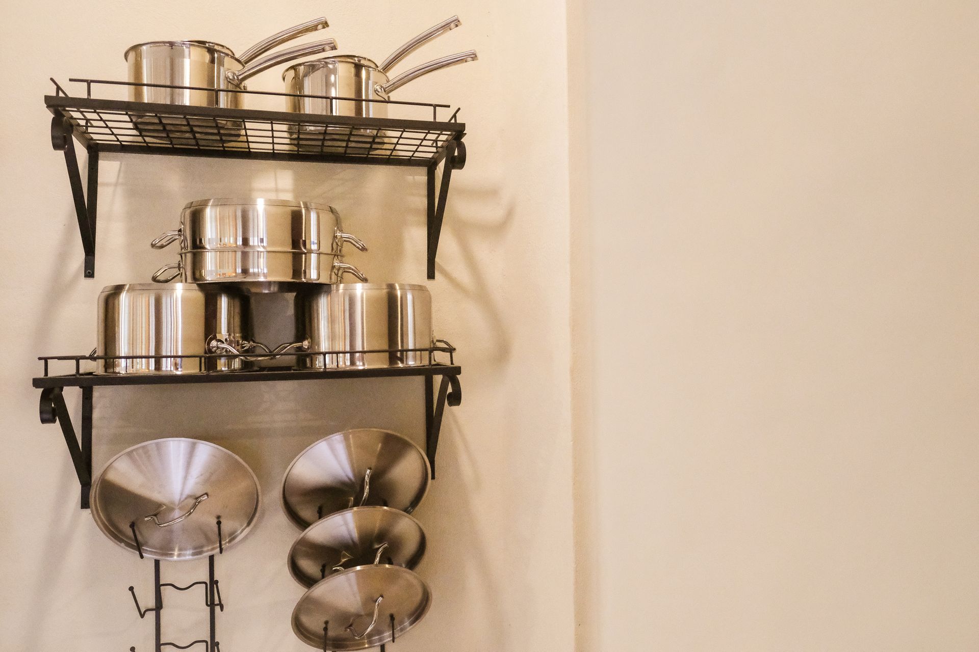 Stainless steel pots and lids organized on a wall-mounted rack in a kitchen.