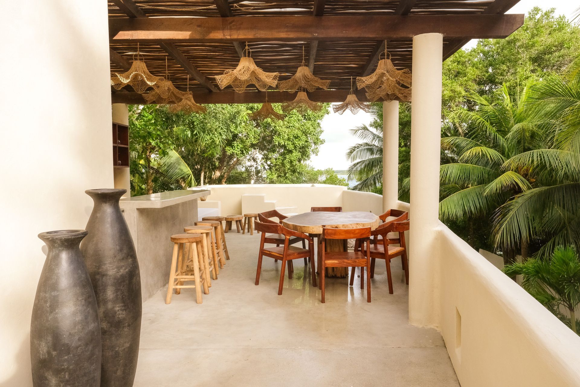 Outdoor patio with wooden furniture, bar, and decorative hanging lights overlooking trees.