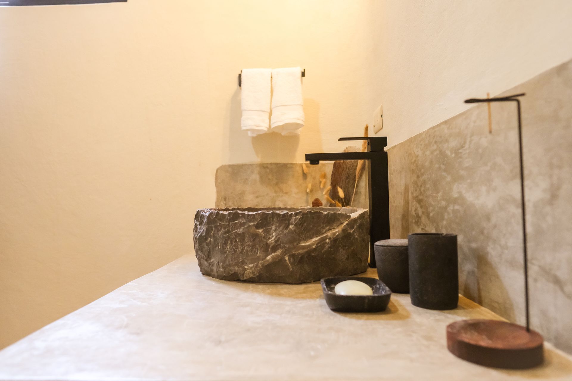 Stone sink and counter in a bathroom with towels, soap dish, and decorative items.