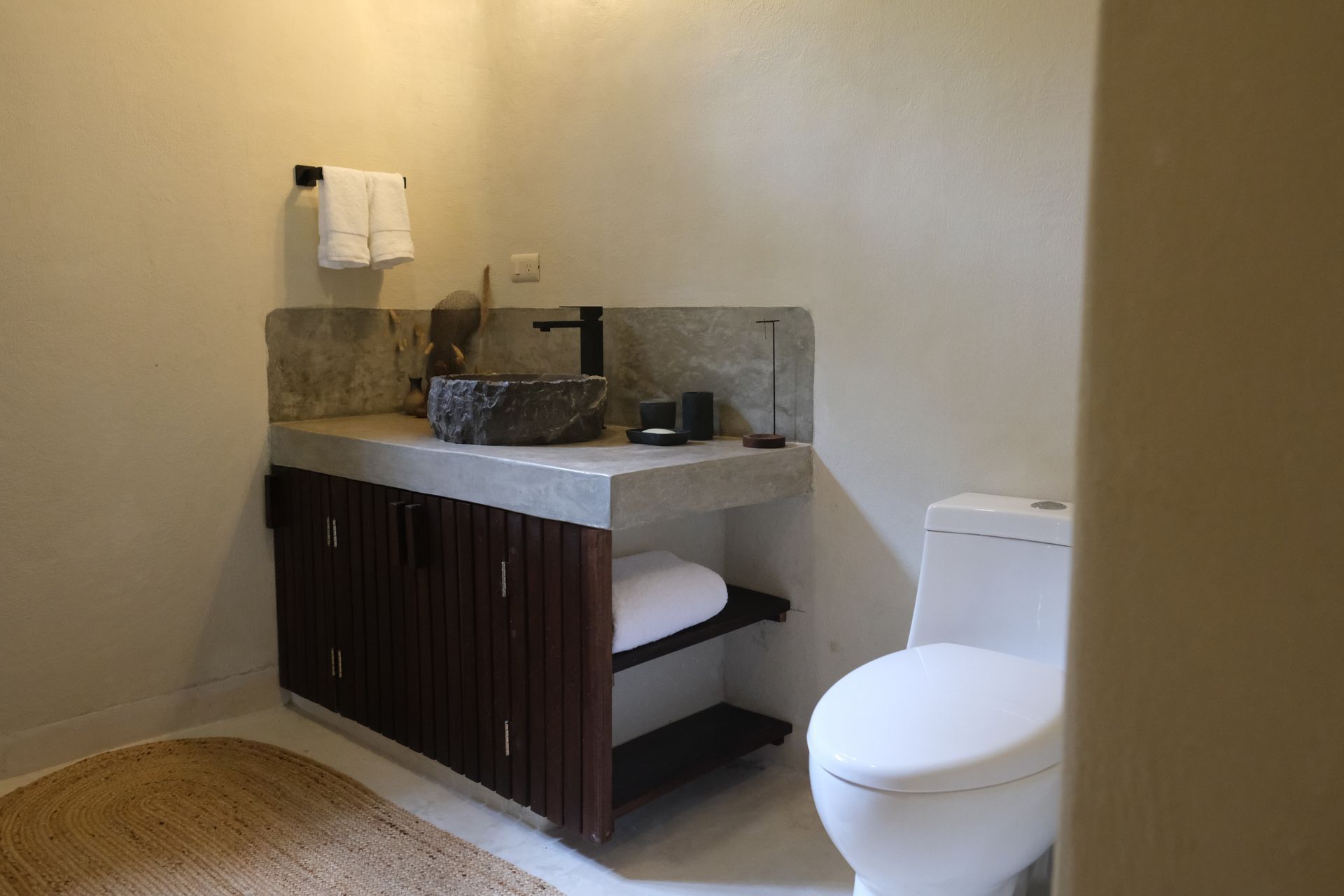 Bathroom with stone sink, wooden cabinet, and white toilet.