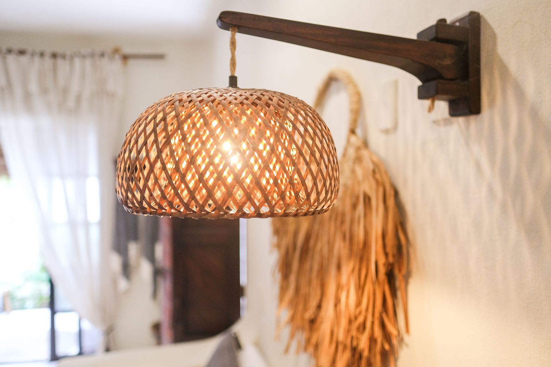 Wall-mounted wooden lamp with woven lampshade, emitting warm light. Decorative wall hanging in the background.